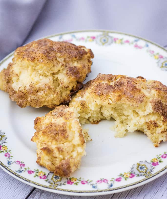 Two cinnamon sugar drop biscuits on a plate, with one biscuit cut in half.