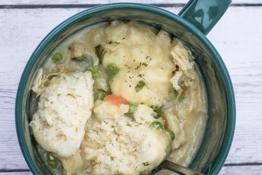 Green bowl filled with chicken and dumplings, with one dumpling split open, showing its fluffy center.
