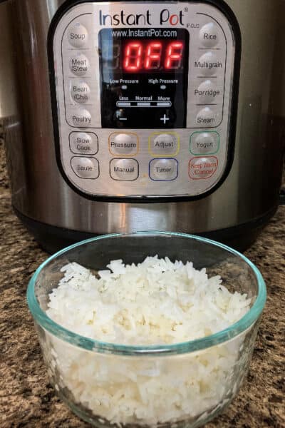 glass bowl of white rice in front of an Instant Pot pressure cooker, showing that rice can be reheated in the Instant Pot