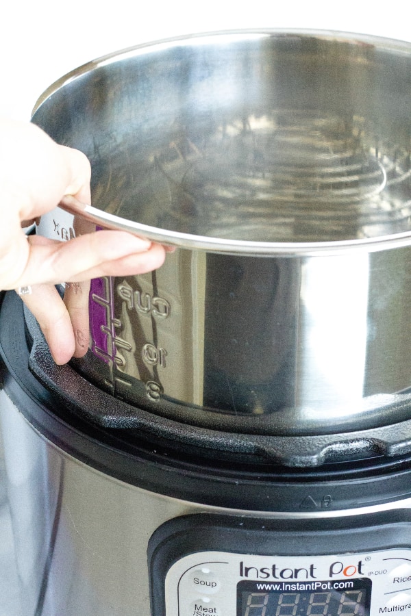 Picture of a hand lowering the insert pot into the Instant Pot, showing you can reheat soup in the Instant Pot by keeping the leftovers in the insert pot.