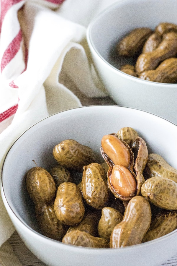 a bowl of boiled peanuts in the shell, with one shell cracked open to reveal two soft peanuts inside