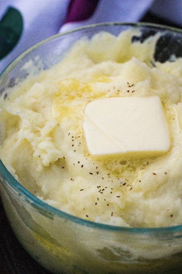 a glass bowl of mashed potatoes with a pat of butter on top