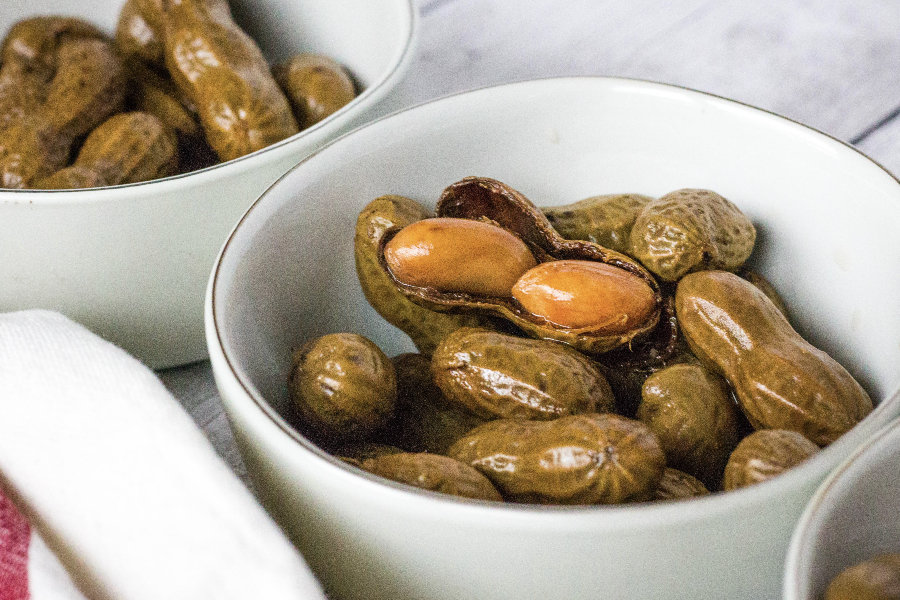 small white bowls filled with boiled peanuts in the shell, with one peanut shell cracked opened to show the tender peanuts inside