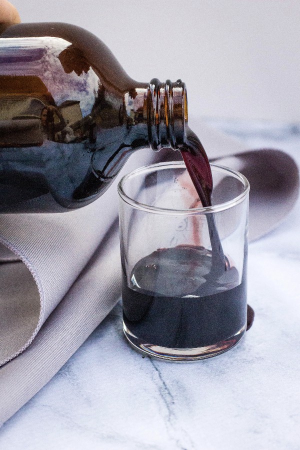 a bottle of elderberry syrup being poured into a small glass