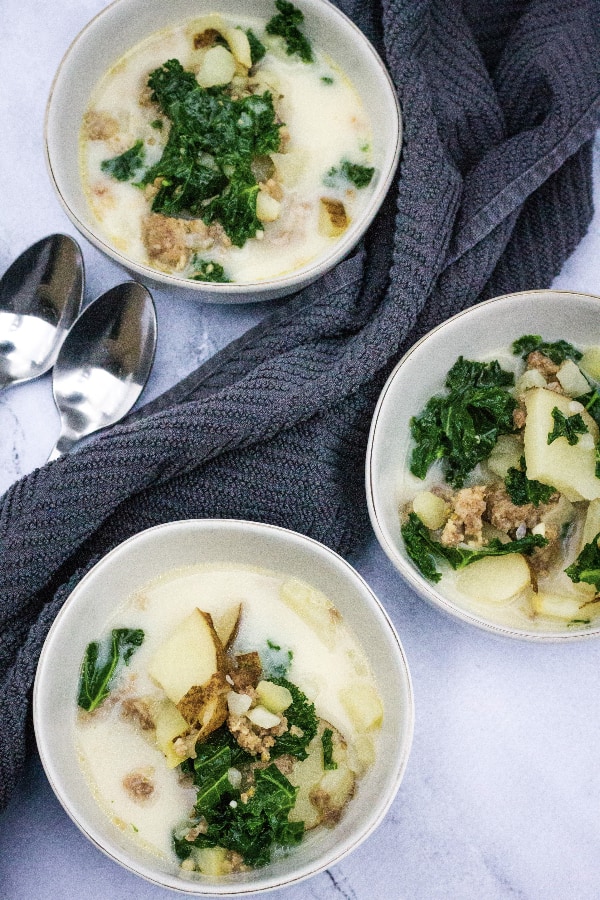 Three white bowls filled with sausage, potato, and kale soup cooked in the Instant Pot