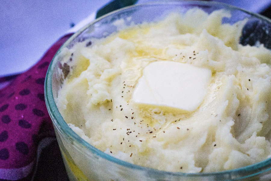 Glass Pyrex dish of mashed potatoes with melted butter that has been reheated in the Instant Pot