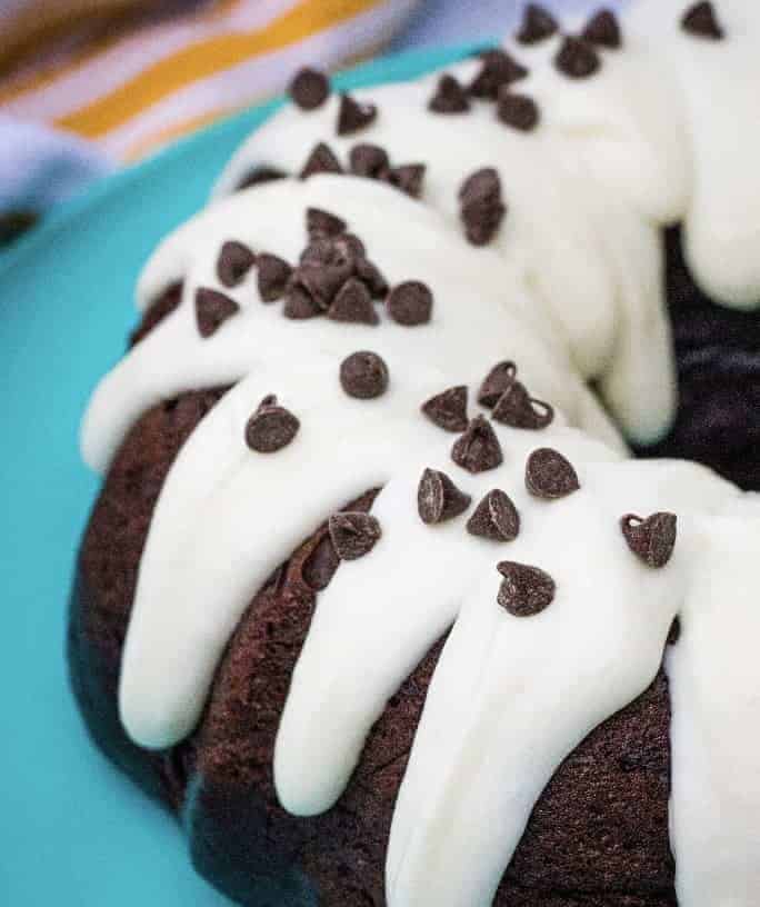 chocolate bundt cake with cream cheese frosting and chocolate chips on a turquoise plate
