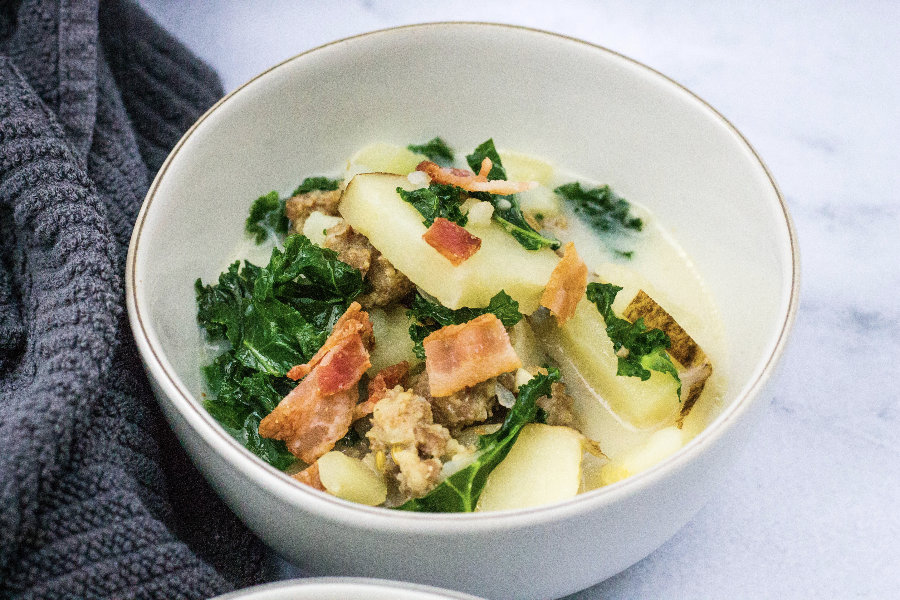 white bowl of healthy zuppa toscana next to a gray kitchen towel