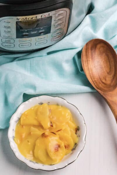 bowl of au gratin potatoes next to an Instant Pot and brown wooden spoon