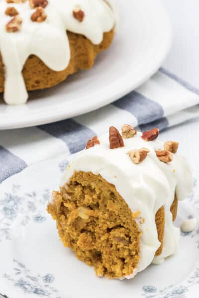 slice of Instant Pot carrot cake on a white and blue plate, with the remaining bundt cake in the background