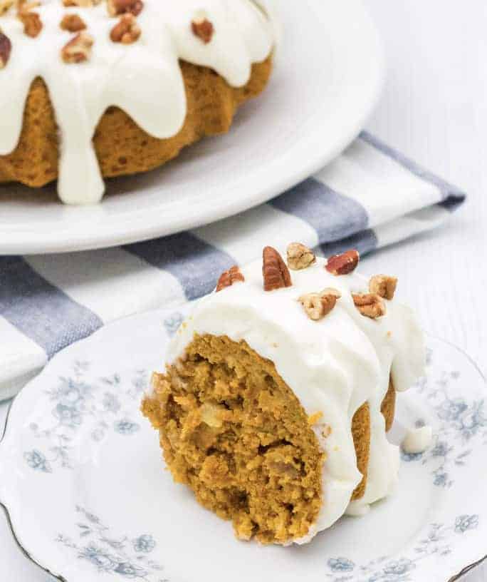 slice of Instant Pot carrot cake on a white and blue plate, with the remaining bundt cake in the background