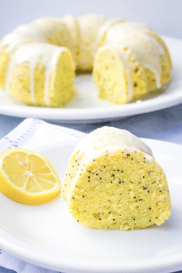 slice of lemon poppy seed bundt cake on a white plate, in front of the whole cake