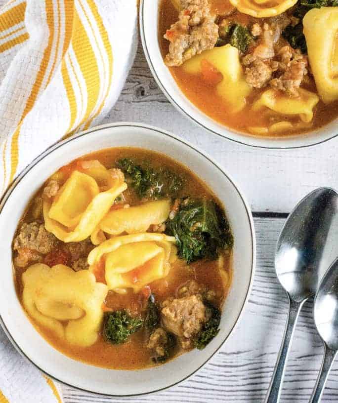 two white bowls of Instant Pot tortellini and sausage soup, next to two spoons