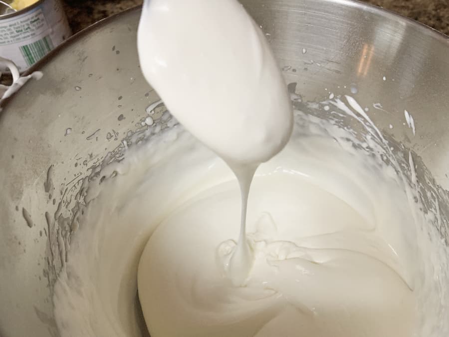Cream cheese frosting for carrot cake in a bowl, dripping off a spoon