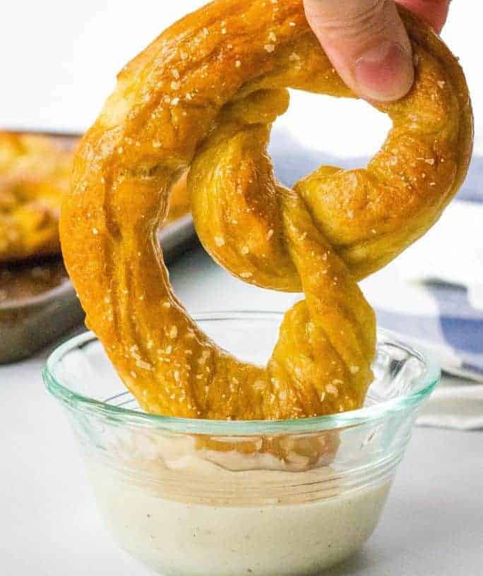 soft baked homemade pretzel being dipped in cheese