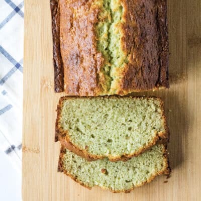 sliced loaf of pistachio banana bread on a light brown cutting board