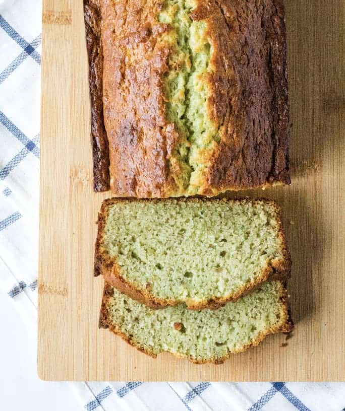 sliced loaf of pistachio banana bread on a light brown cutting board