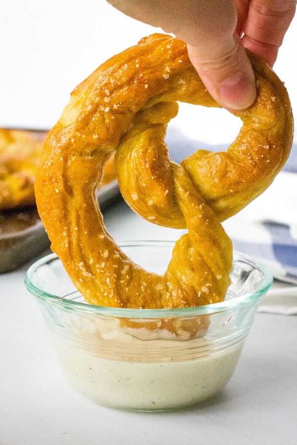 homemade soft pretzel being dipped into a bowl of cheese sauce