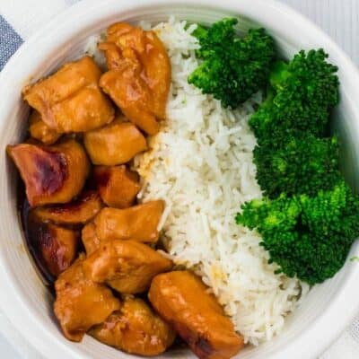 white bowl of teriyaki chicken, rice, and broccoli on a blue and white striped cloth