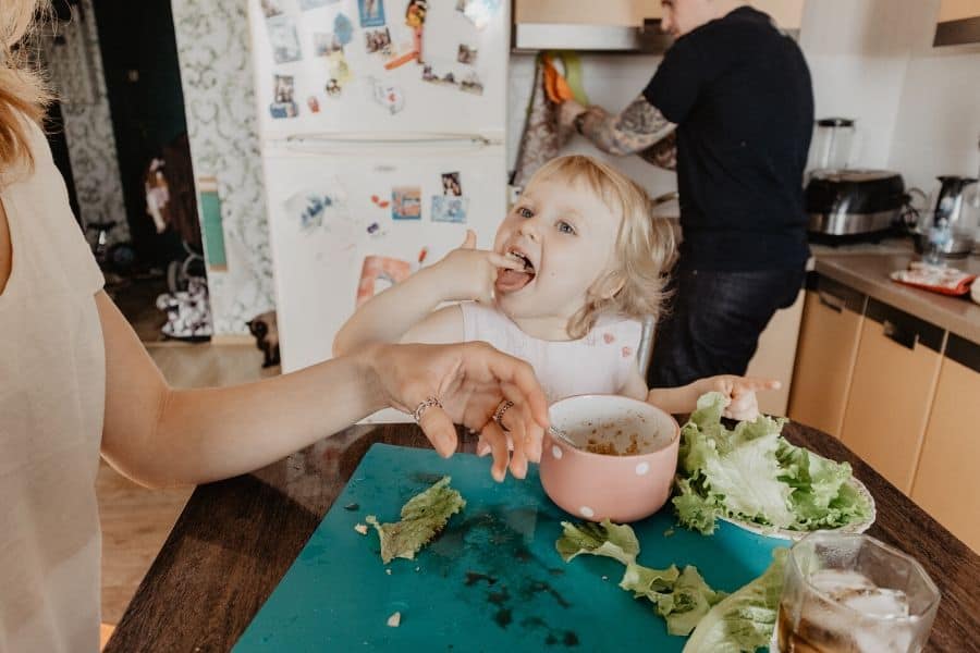 young girl eating lettuce and chili with her mom