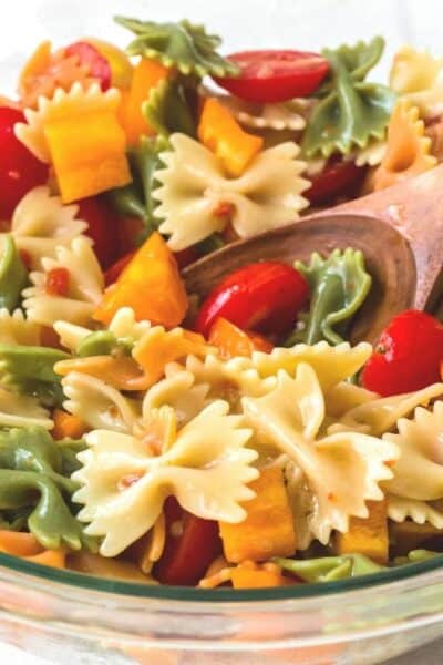 bowl of italian pasta salad with a wooden spoon scooping some out