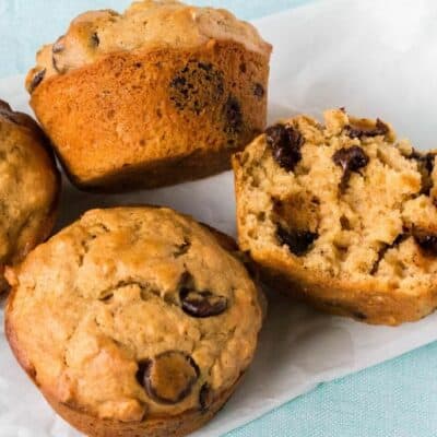 several oatmeal chocolate chip muffins on a piece of parchment paper, with one muffin cut open