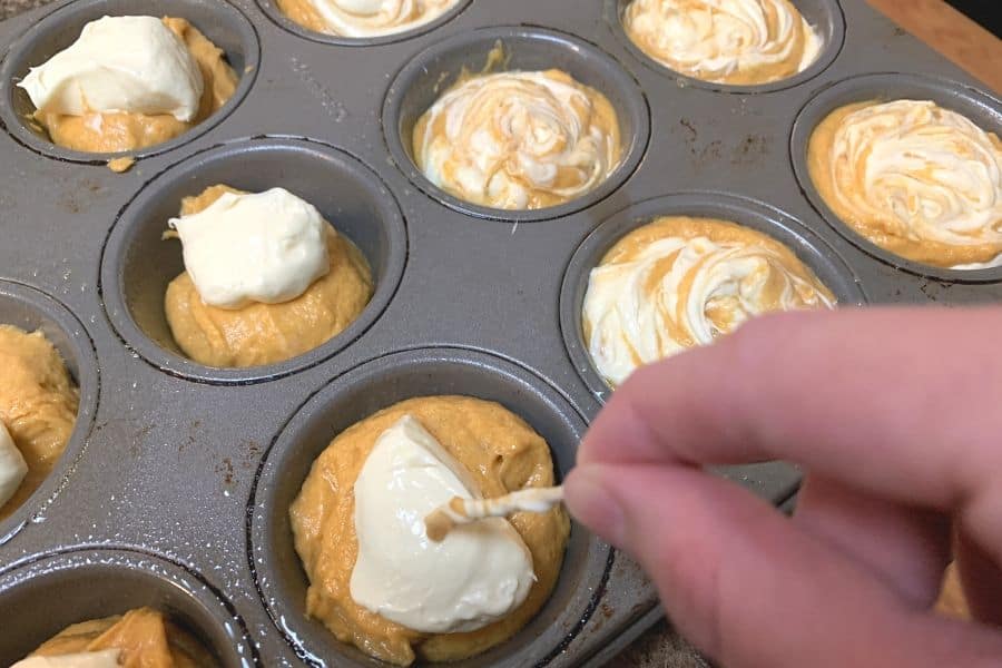 a hand using a toothpick to swirl cream cheese filling into the pumpkin muffins