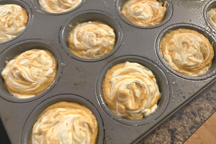 a muffin pan filled with pumpkin cream cheese muffin batter, ready to be transferred to the oven