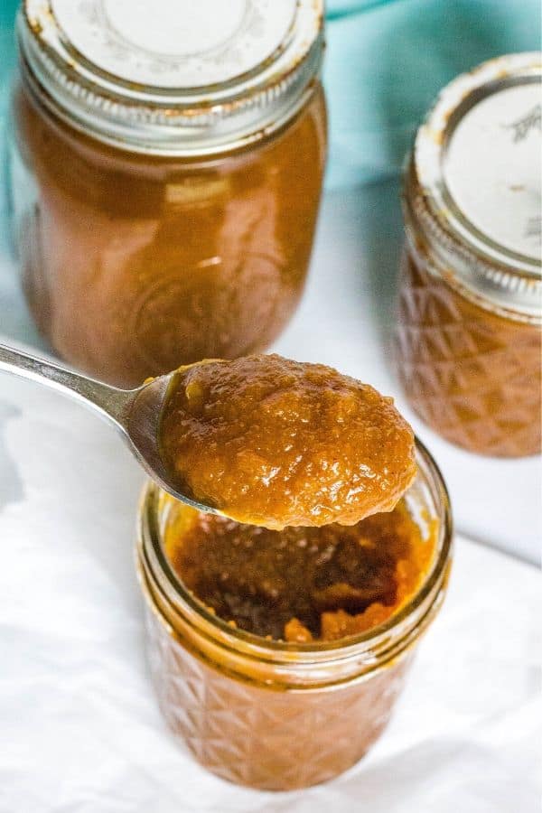 jars filled with pressure cooker pumpkin apple butter, with a spoon removing a scoop