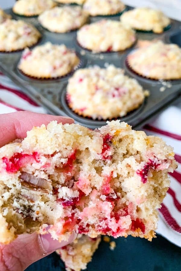 half of a cranberry orange pecan muffin in the foreground with a pan of muffins in the background