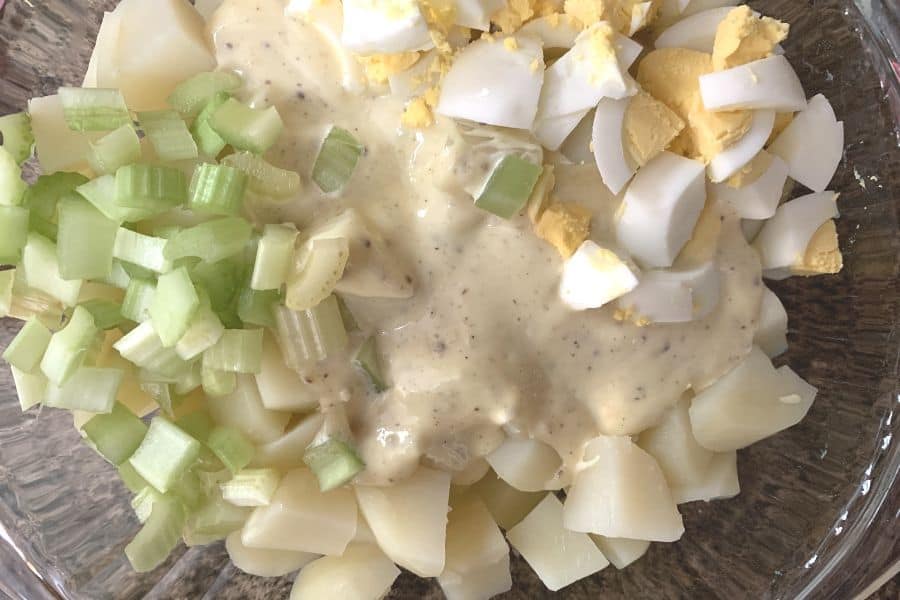 Combining dressing, potatoes, eggs, and celery in a mixing bowl