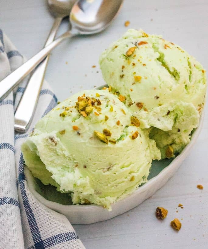 white custard cup filled with homemade no-churn pistachio ice cream and garnished with chopped pistachios