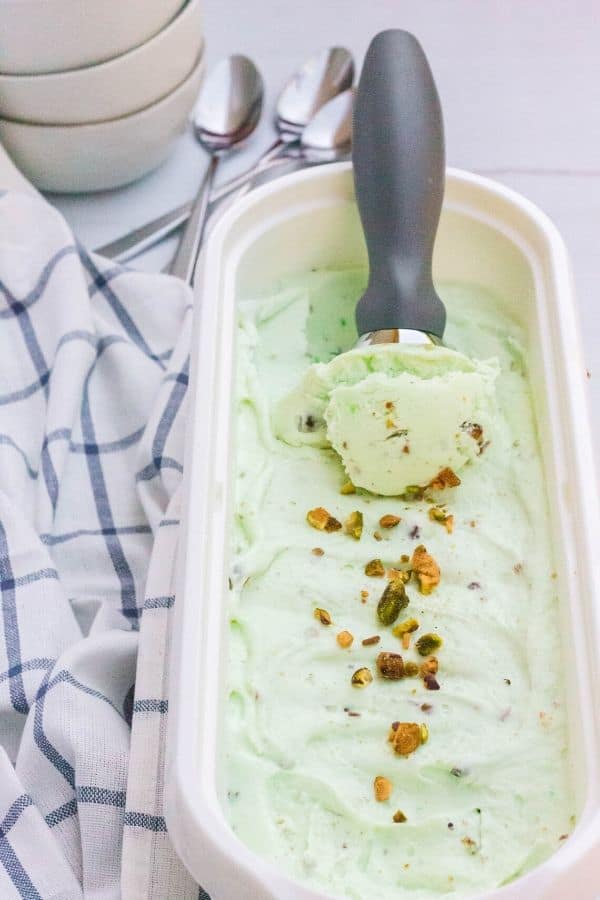 a full container of no-churn pistachio ice cream, with an ice cream scoop removing a curl of ice cream
