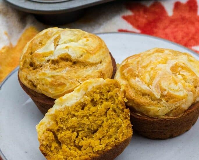 three pumpkin cream cheese muffins on a plate in front of a muffin tin