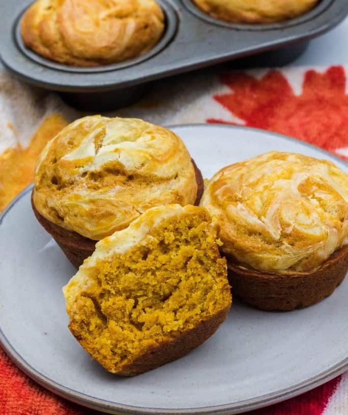 three pumpkin cream cheese muffins on a plate in front of a muffin tin