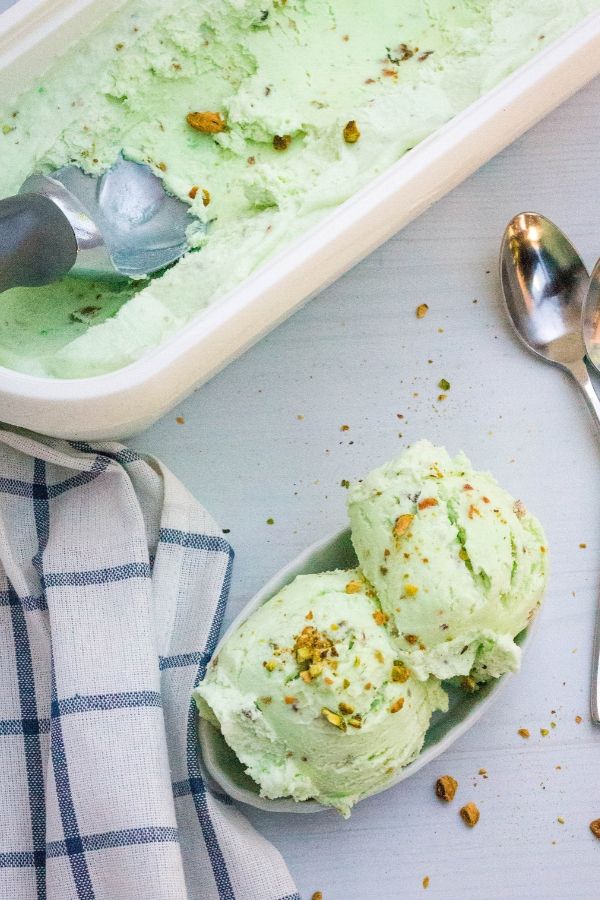 a dessert dish filled with scoops of pistachio ice cream, next to the entire container of the batch of ice cream