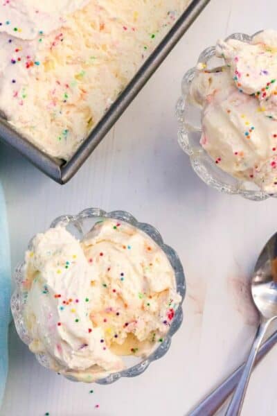 two dessert cups with scoops of homemade cake batter ice cream next to the serving dish of ice cream