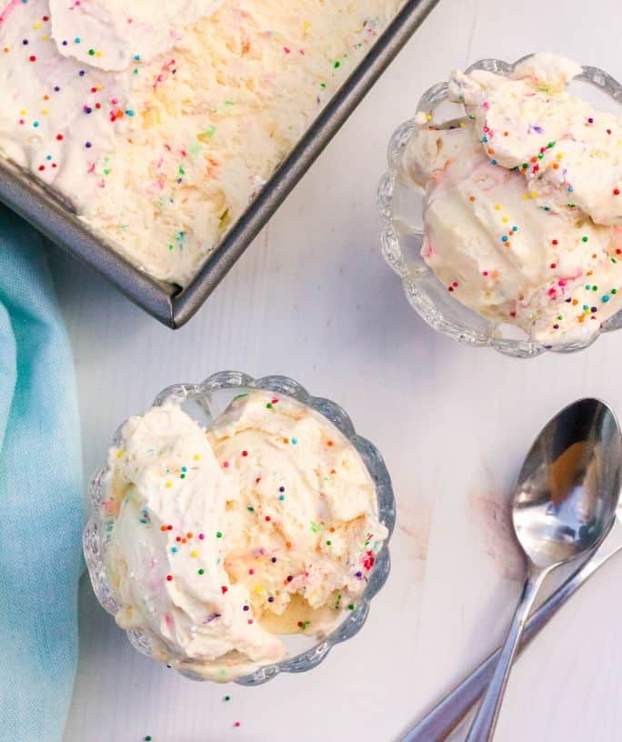 two dessert cups with scoops of homemade cake batter ice cream next to the serving dish of ice cream