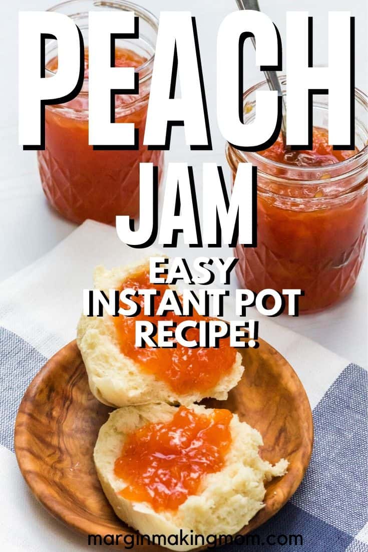 a dinner roll slathered with Instant Pot peach jam, on a wooden plate in front of two jars of jam