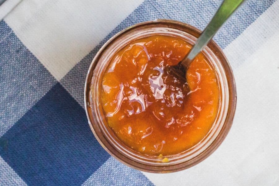 peach jam in a jar, with a spoon in the jar