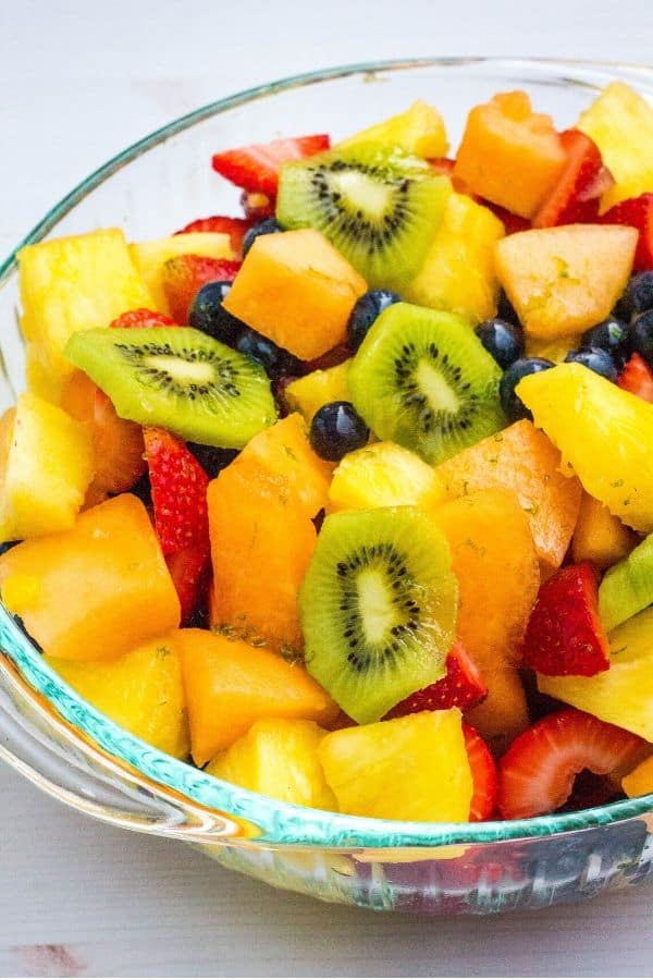 glass bowl full of fruit salad mixed with honey lime dressing