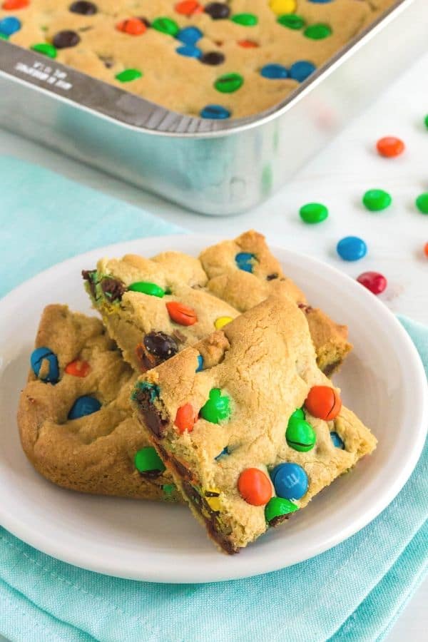 a pan of M&M cookie bars next to a white dessert plate with a few bars on it