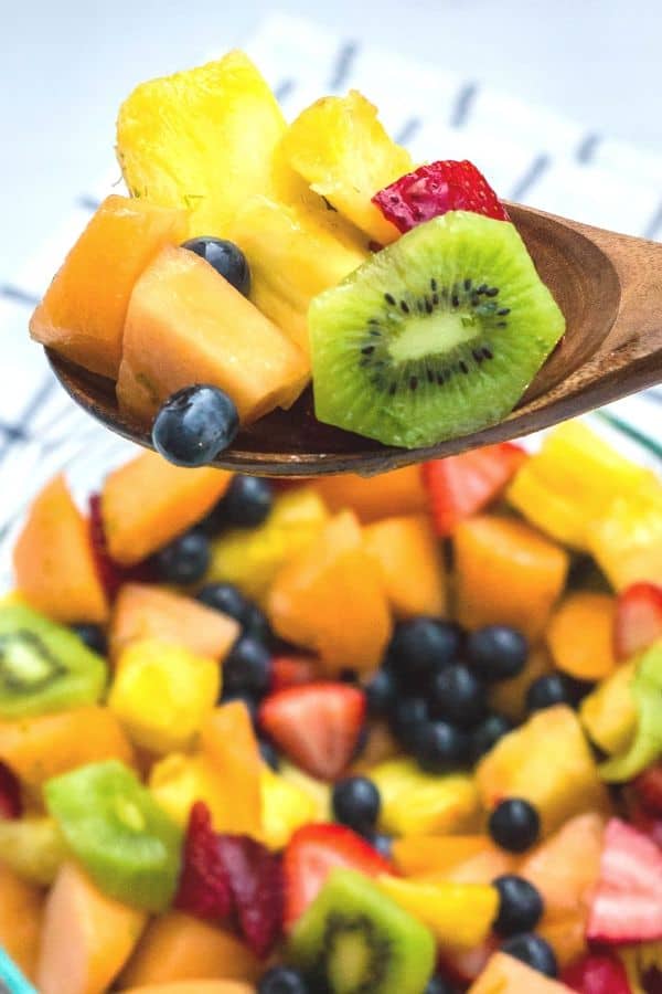 Wooden serving spoon with a scoop of honey lime fruit salad on it