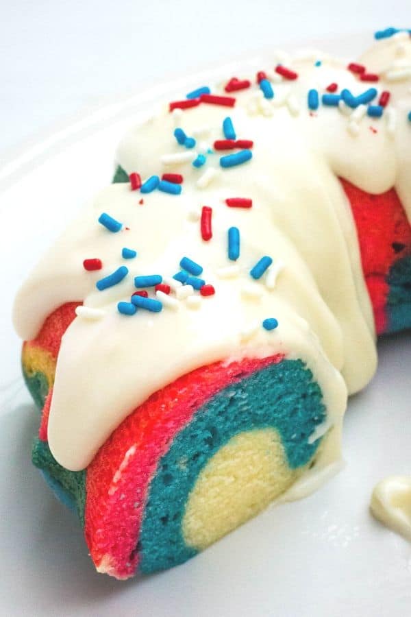 section of a patriotic bundt cake, with red, white, and blue swirls throughout, topped with cream cheese glaze and patriotic sprinkles