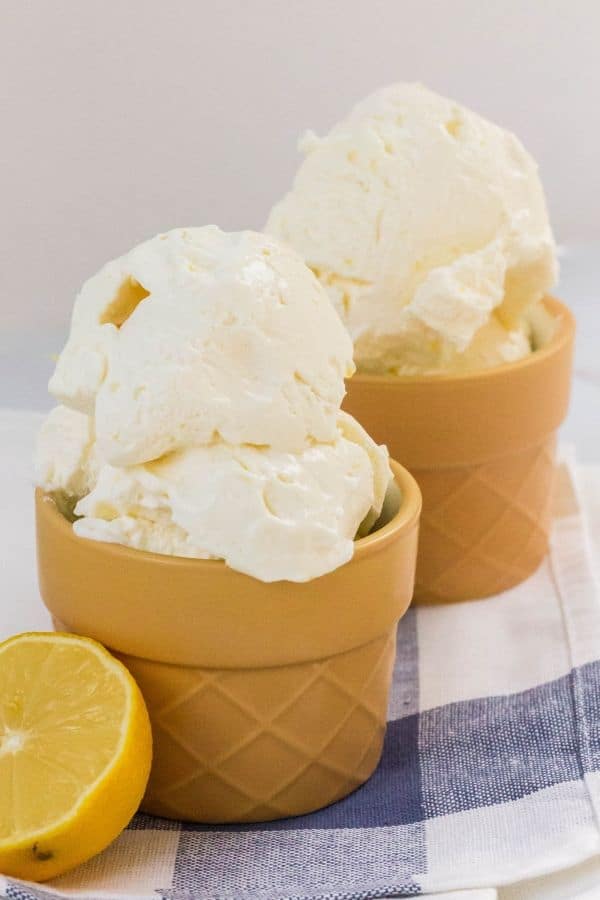 two dessert cups filled with scoops of homemade lemon ice cream, with a halved lemon next to one of the cups