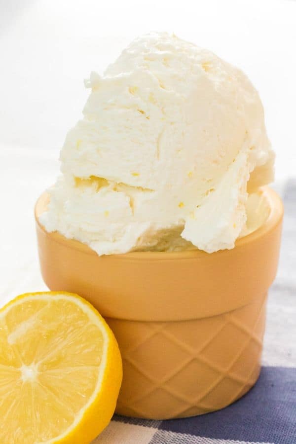 a scoop of homemade no-churn lemon ice cream in a small dessert cup, with half of a lemon next to it