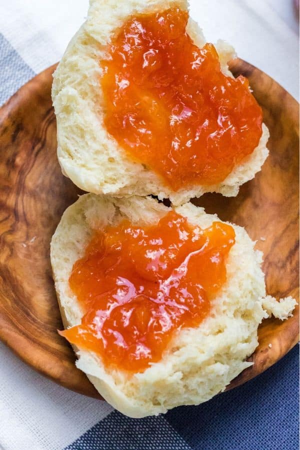 two biscuit halves on a small wooden plate, each topped with homemade peach jam with skins