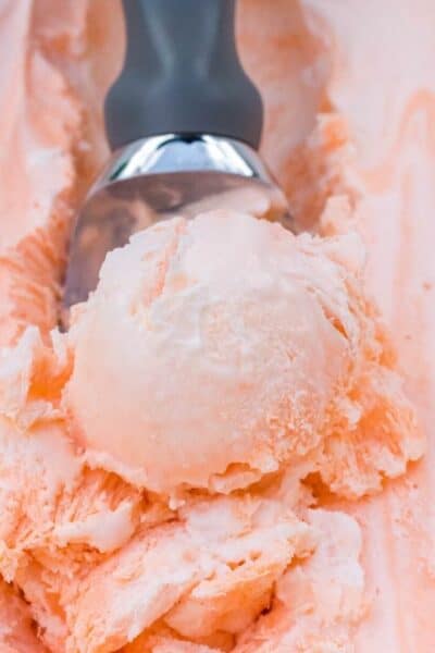 freezer container of orange soda ice cream with a scoop removing a serving