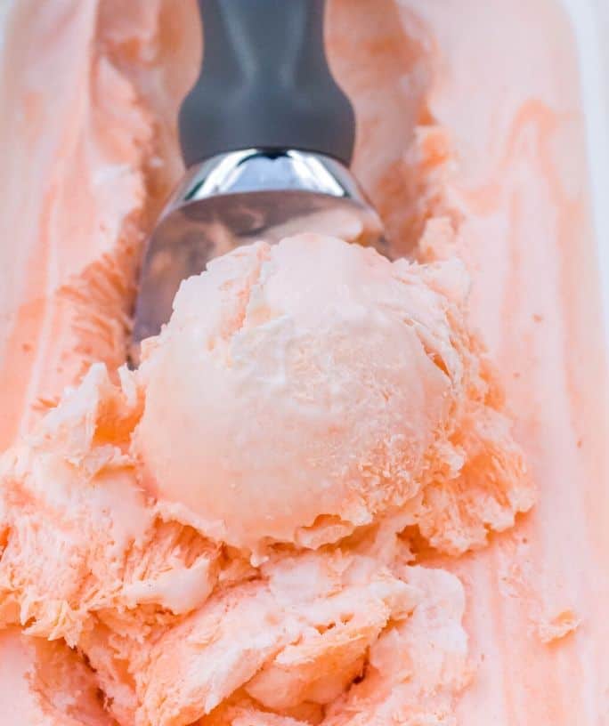 freezer container of orange soda ice cream with a scoop removing a serving