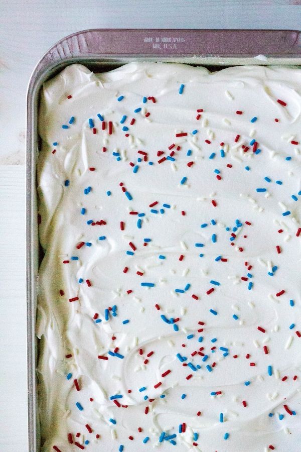 the top (overhead view) of a patriotic poke cake, with whipped cream and red, white, and blue sprinkles
